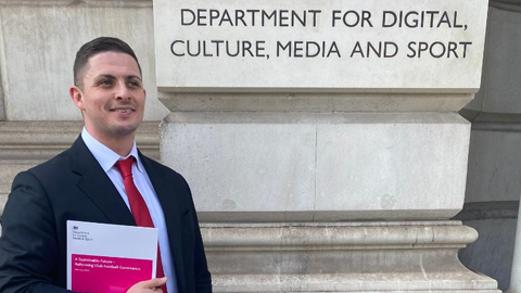 Jonny standing holding papers next to a sign for the Department for Digital, Culture, Media and Sport.