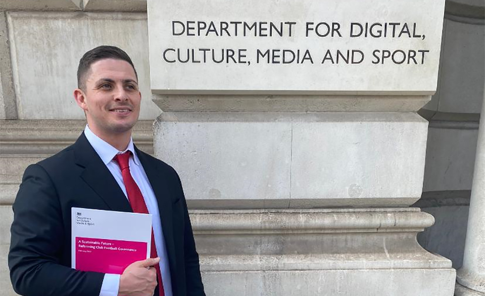 Jonny standing holding papers next to a sign for the Department for Digital, Culture, Media and Sport.