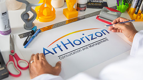 A piece of paper on a desk with drawing supplies that has the ArtHorizon logo on.