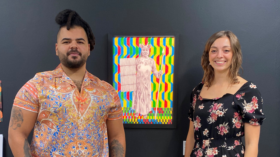 Habib and Rebecca standing together with a piece of art featuring a person in the centre. In the background of the artwork there are colourful shapes. Image courtesy of Reece Straw.
