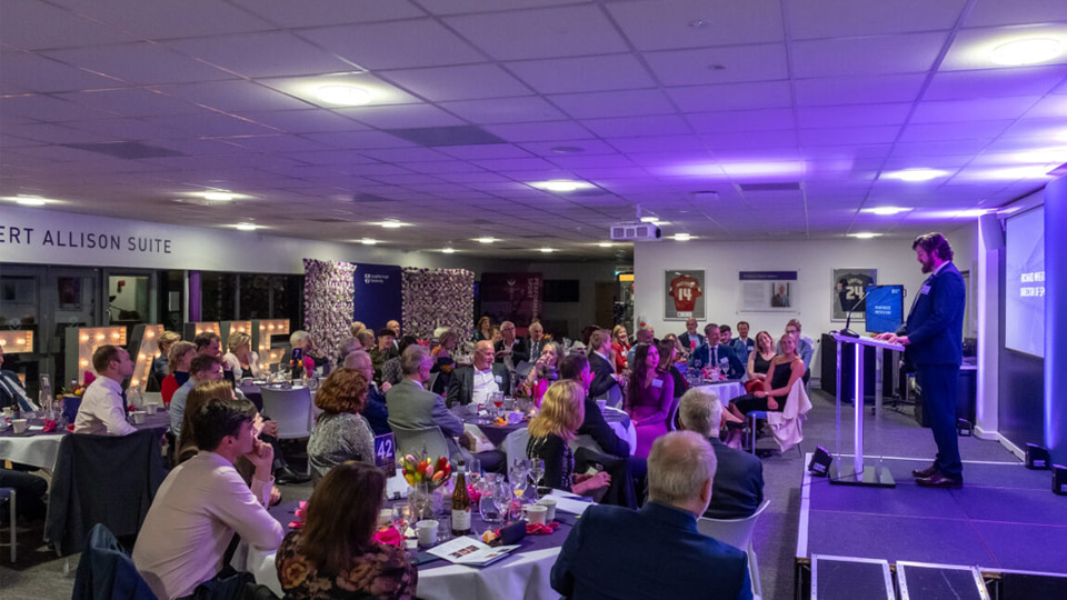 Richard Wheater on stage in front of a room of people seated at tables