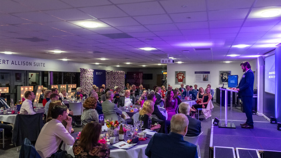 Richard Wheater on stage in front of a room of people seated at tables