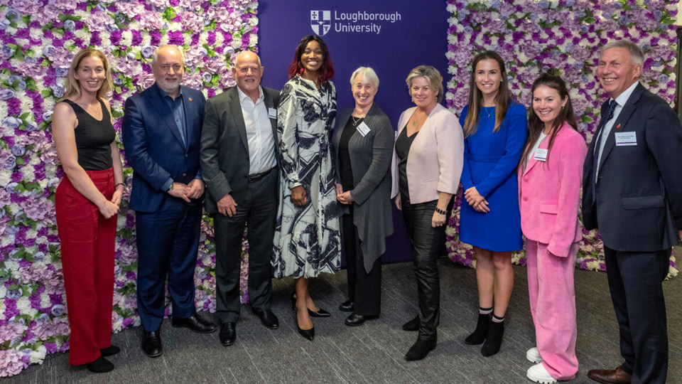 A group of Hall of Fame members and the Vice-Chancellor stand together smiling in front of a purple backdrop and flower backdrops.