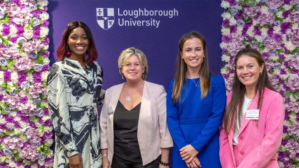 Ama Agbeze, Amanda Bennett, Maddie Hinch, and Laura Unsworth stand together smiling in front of a purple backdrop and flower backdrops.