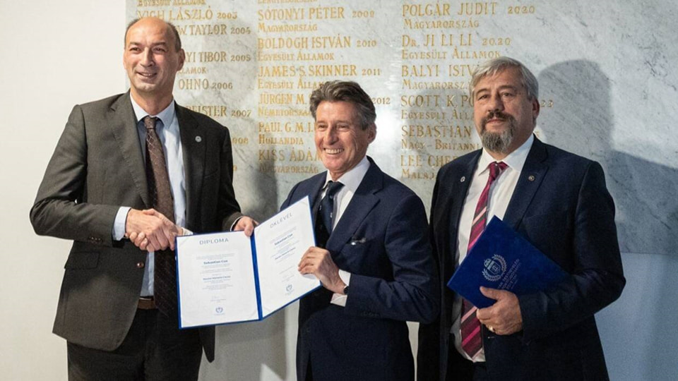 Lord Coe holding a certificate. He stands in between two other men.