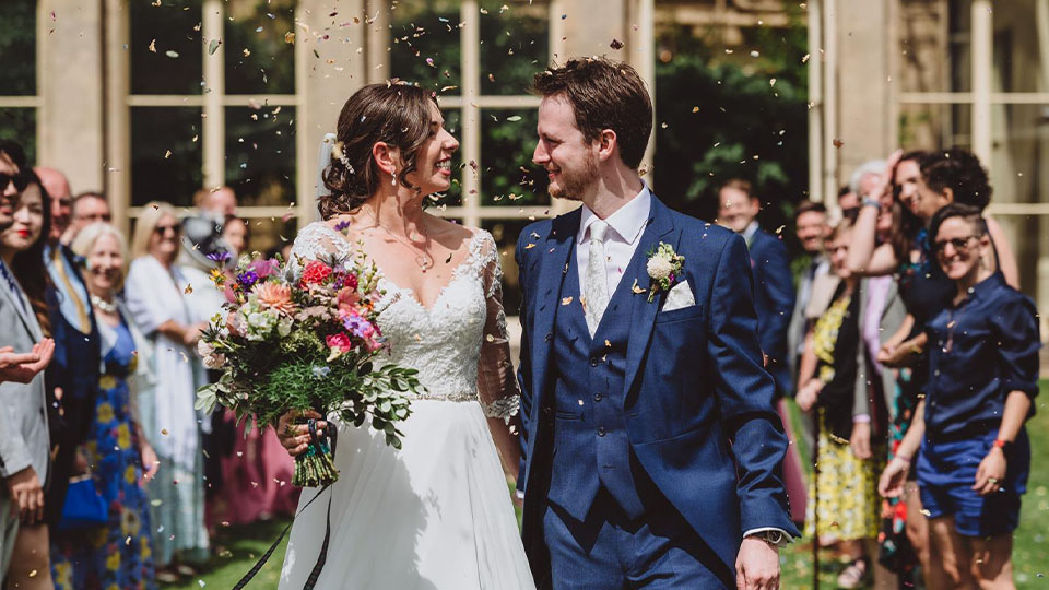 Lizzie and Lewis on their wedding day standing under confetti.