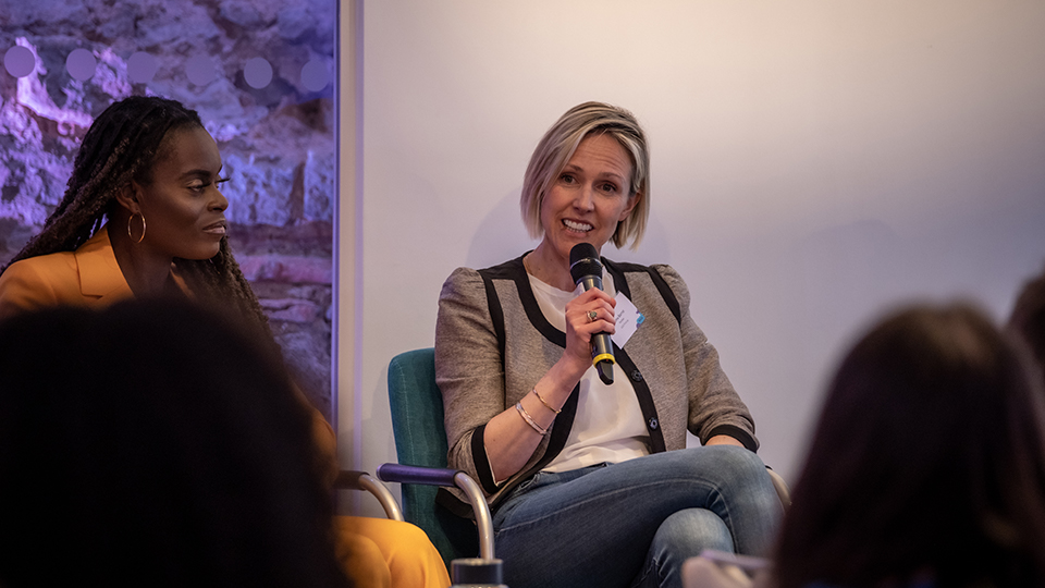 Emma Barrat speaking into a microphone. She is seated. Another person is seated to the left. 