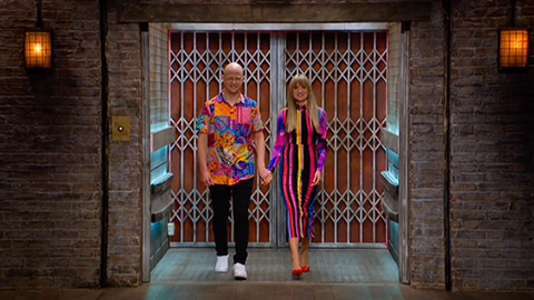 Simon and Charlene stepping out of the Dragons' Den lift. Both wear colourful clothes.