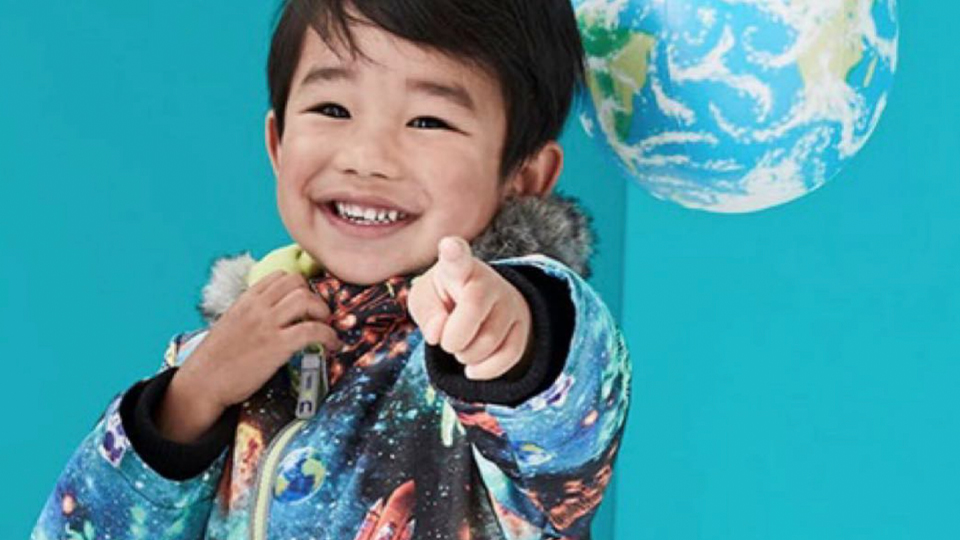 A child smiling and pointing wearing a jacket with charlotte wills designs and pointing