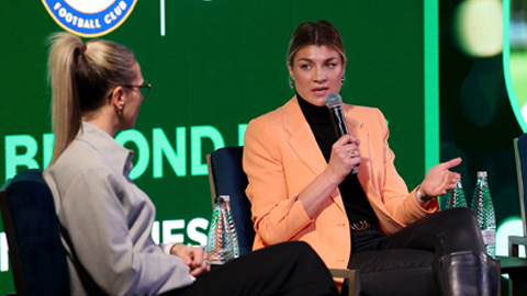 Flo Edwards seated on a stage with a microphone, talking