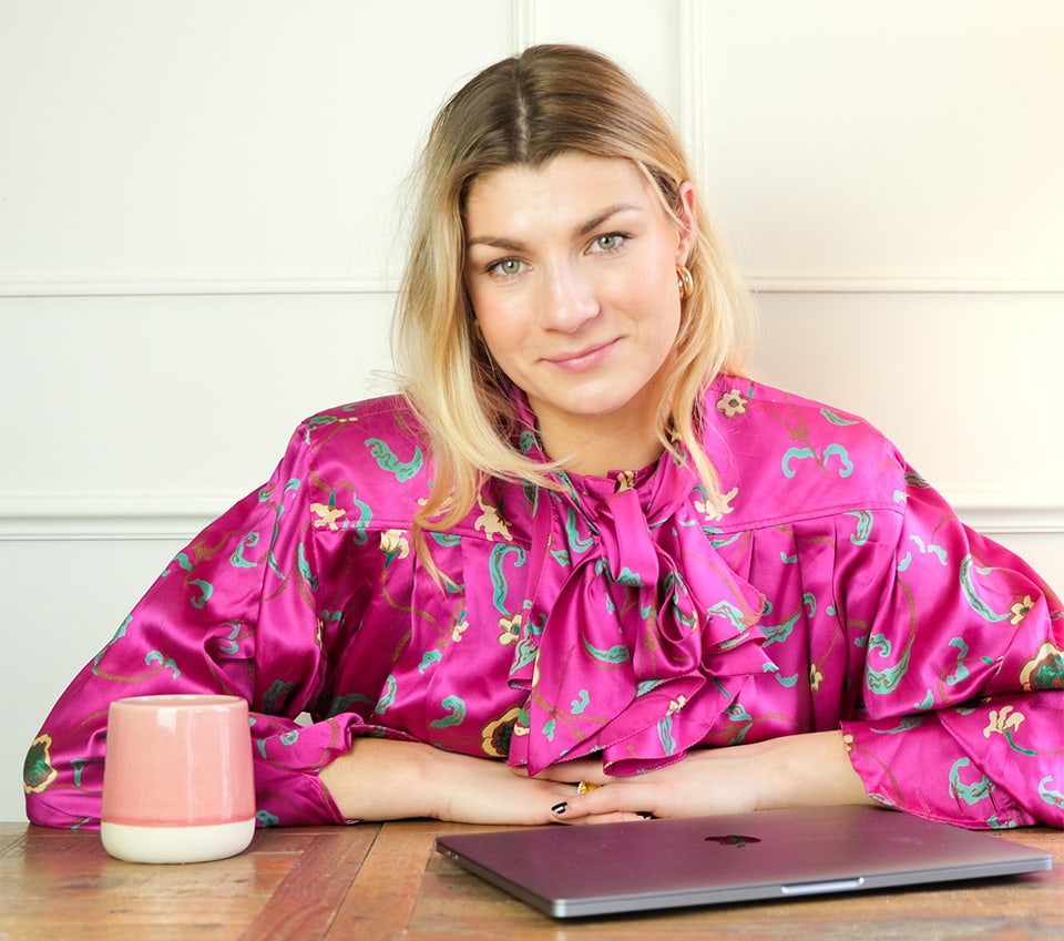 Flo Edwards with her arms on a desk. There is a mug and a laptop on the desk.