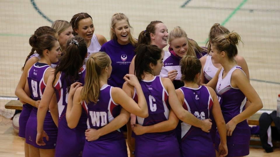 A group of people wearing purple netball kit are huddle in a circle.