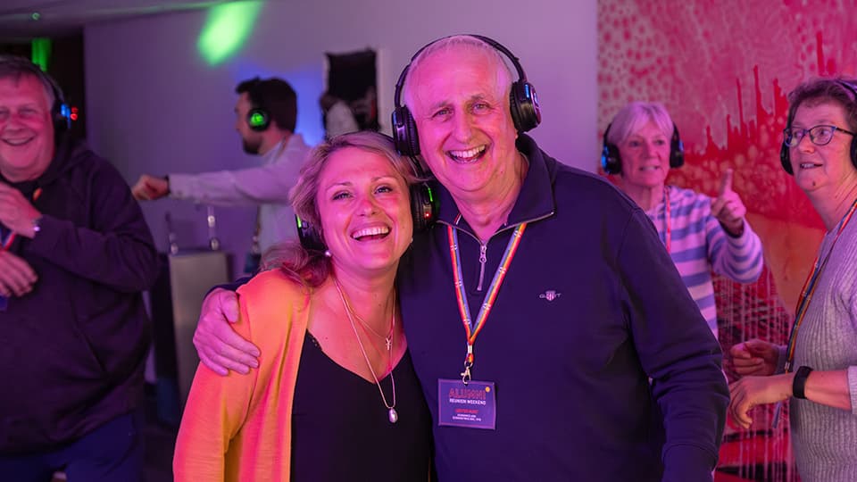 Two people wearing headphones, smiling to the camera