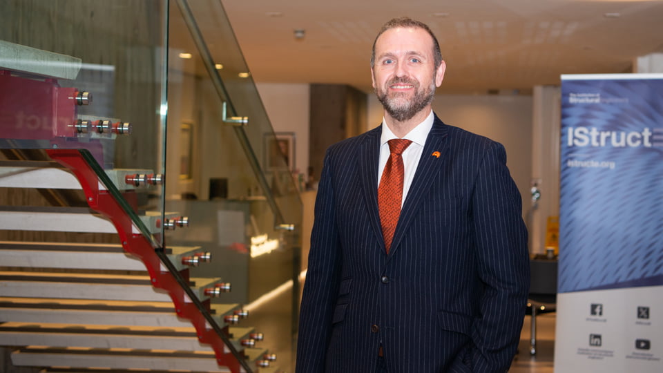 keith Williams wearing a suit, standing near stairs. There is an IStruct banner behind him.