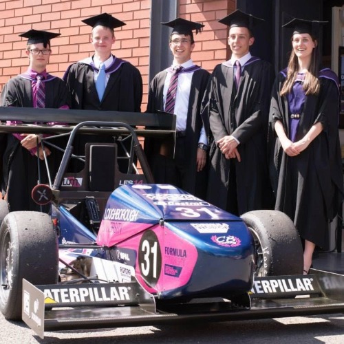 Holly stands with others in graduation attire, the LU Motorsport car is in the image