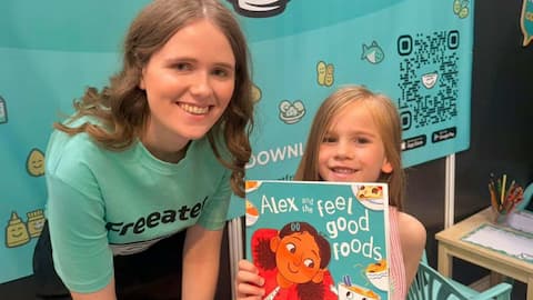Kate standing with a child who is holding the Alex and the feel good foods book