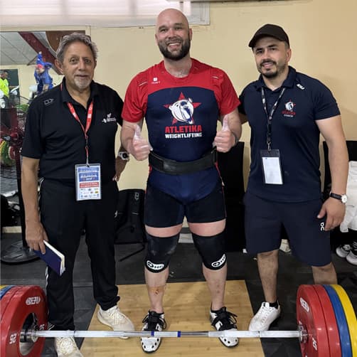 Three people standing in a gym with a set of weights