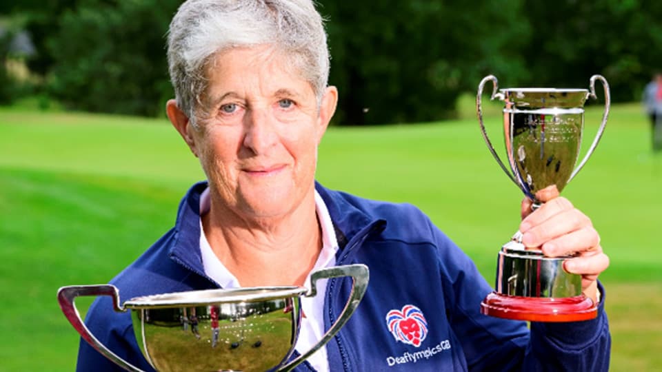 Karen Ellam holding two trophies, wearing a Deaflympics GB tracksuit top