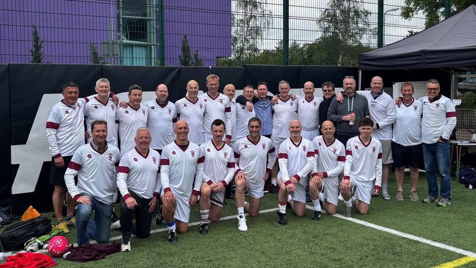 A group of people crouched and standing together. They are wearing white football kits.
