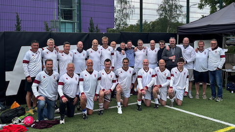 A group of people crouched and standing together. They are wearing white football kits.