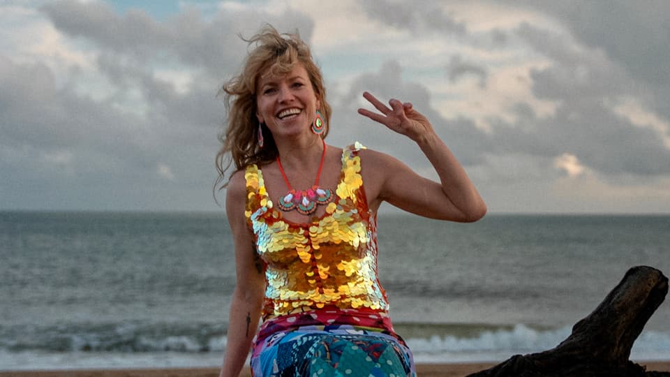 Lindsey wearing a sequined mermaid outfit, perched by the sea.