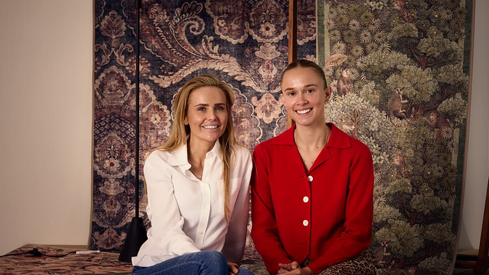 Two people - Ellie and Iona - seated surrounded by their rug designs.