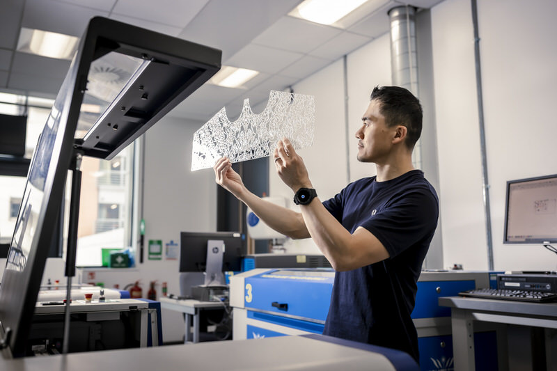A male researcher in a lab wearing a black shirt holding up a piece of glass.