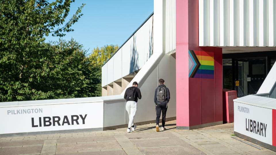 Two students walking into the entrance of the Pilkington Library on campus.