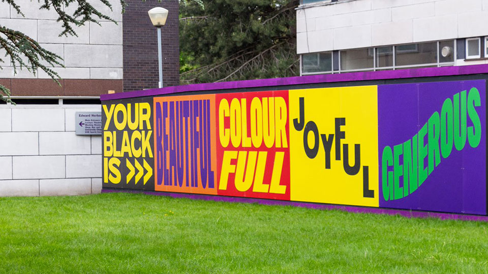 A colourful mural reading 'Your Black Is' and a row of positive words along a panel on campus.