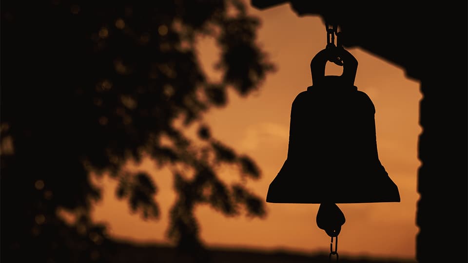 a silhouette of a large bell in the sunset