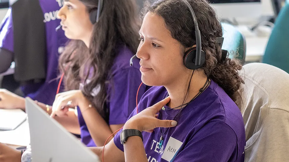 University staff members wearing purple t-shirts and headsets working at laptops in a busy call centre.