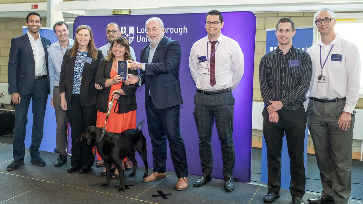 Eight members of the student finance PMB, and Pickle the Guide Dog, receiving their VC Award from the Vice-Chancellor, Nick Jennings