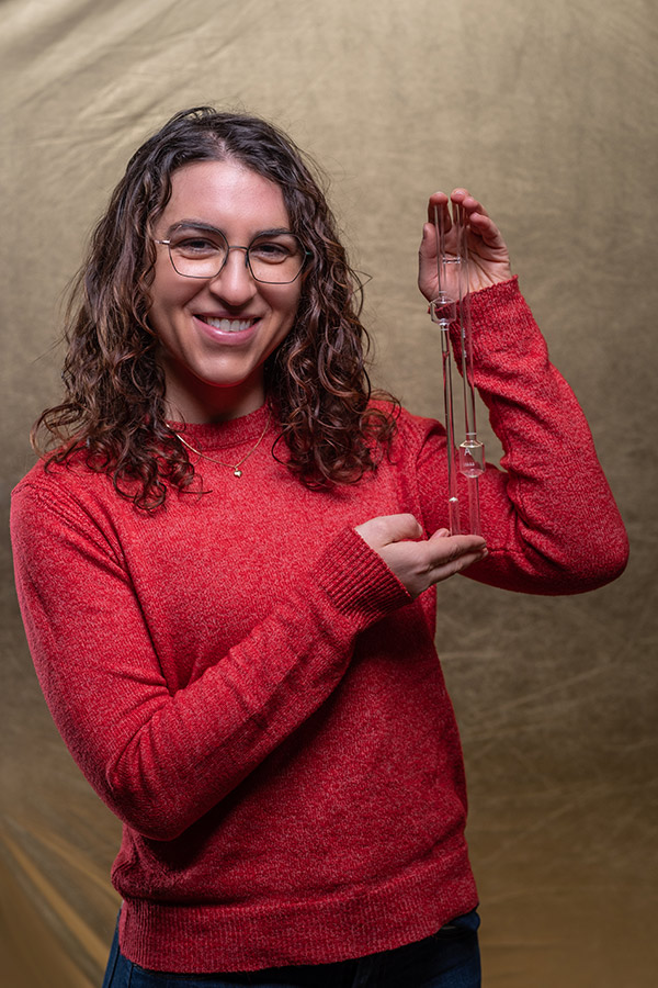 Dr Amanda Pearce stood holding a glass Ubbelohde U-tube viscometer. 