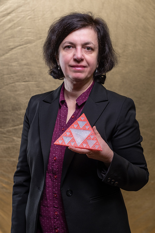 Dr Ana Salagean holding a red and white object in the shape of a triangle with Pascal's triangle modulo 2 pattern printed onto it. 
