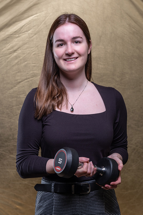 Emily Hansell stood holding a dumbbell between two hands in front of her. 