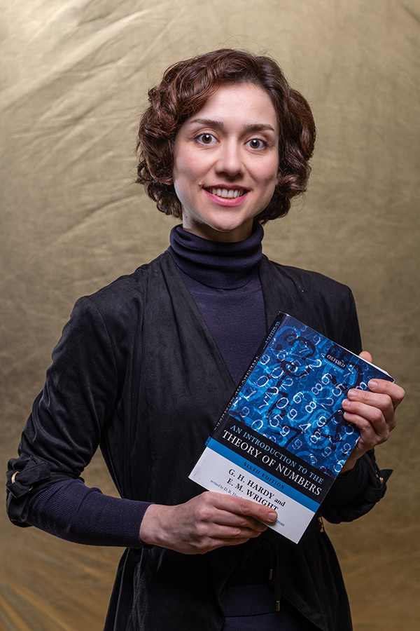 Dr Parisa Derakhshan stood holding a book written by G. H. Hardy and E. M. Wright entitled 