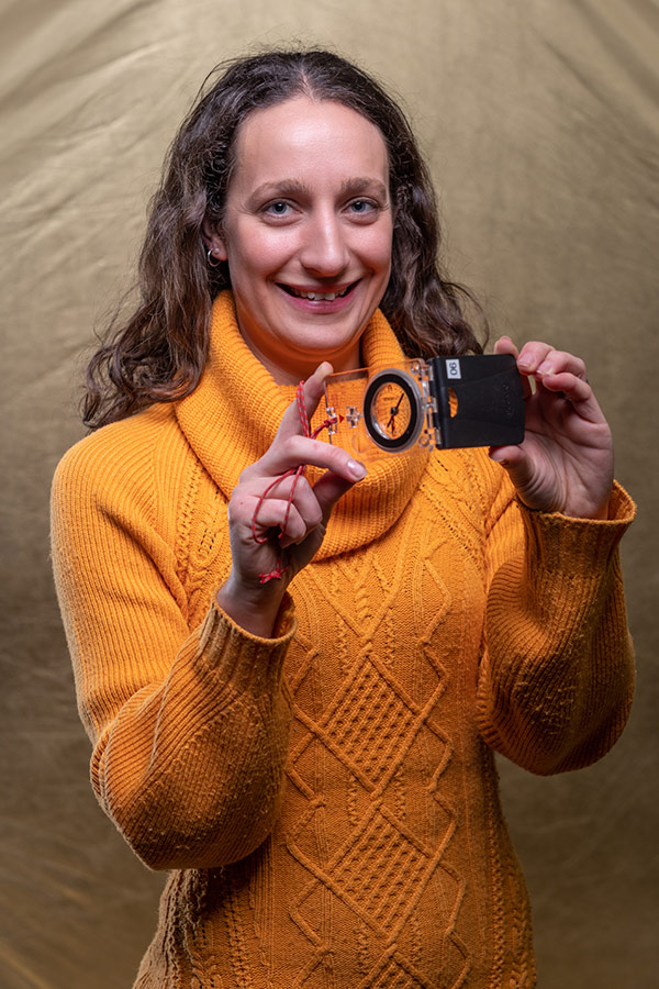 Dr Sarah Wappat is stood holding a compass clinometer between her hands. 