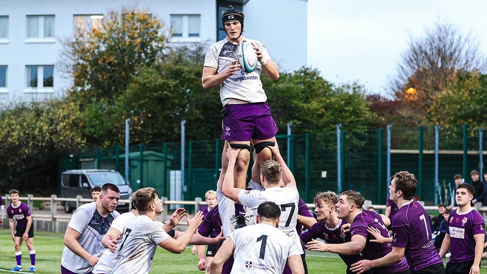 Men's rugby union match in progress with one player being held up in the air holding the ball