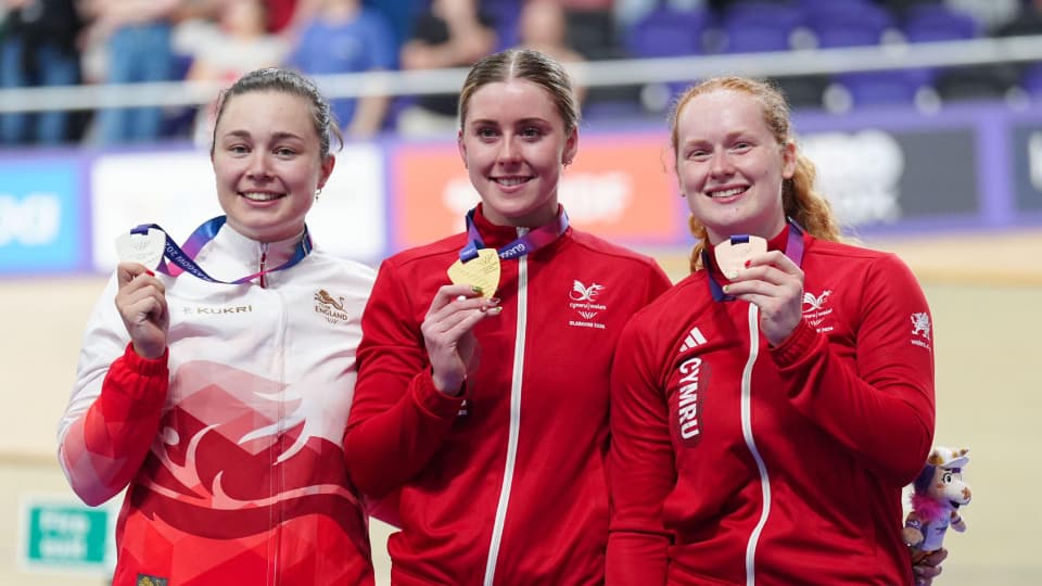 Sophie Capewell,Emma Finucane and Rhian Edmunds on the podium holding medals, wearing tracksuits