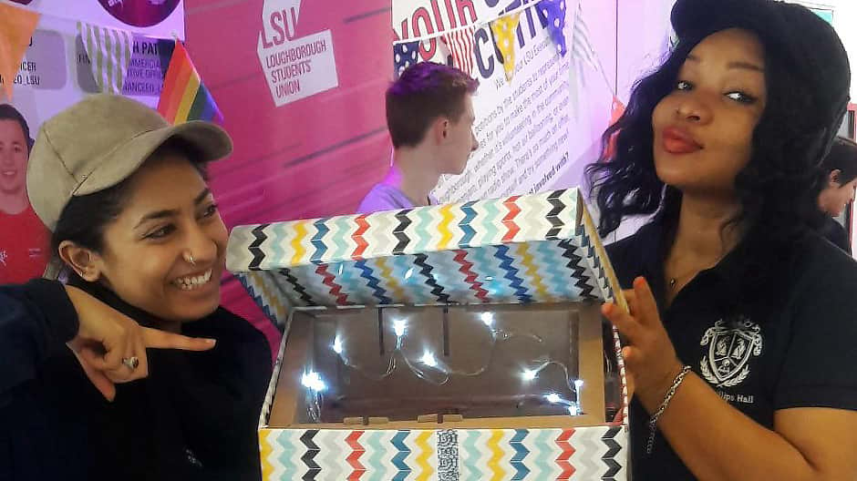 two students in the Students' Union, one holds a box with led lights and other other points and smiles