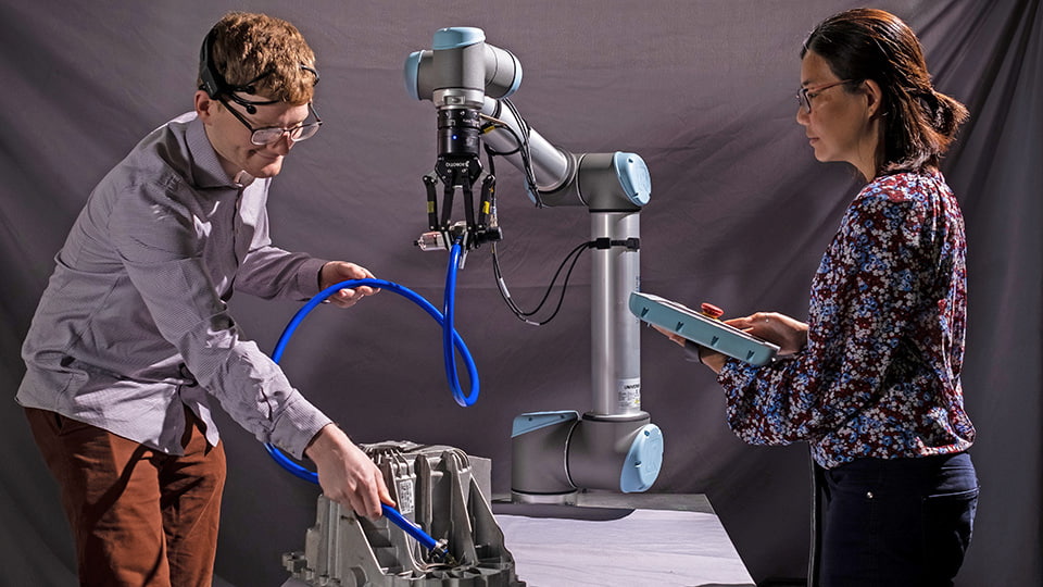 Two researchers standing either side of a robotic arm carrying out a test