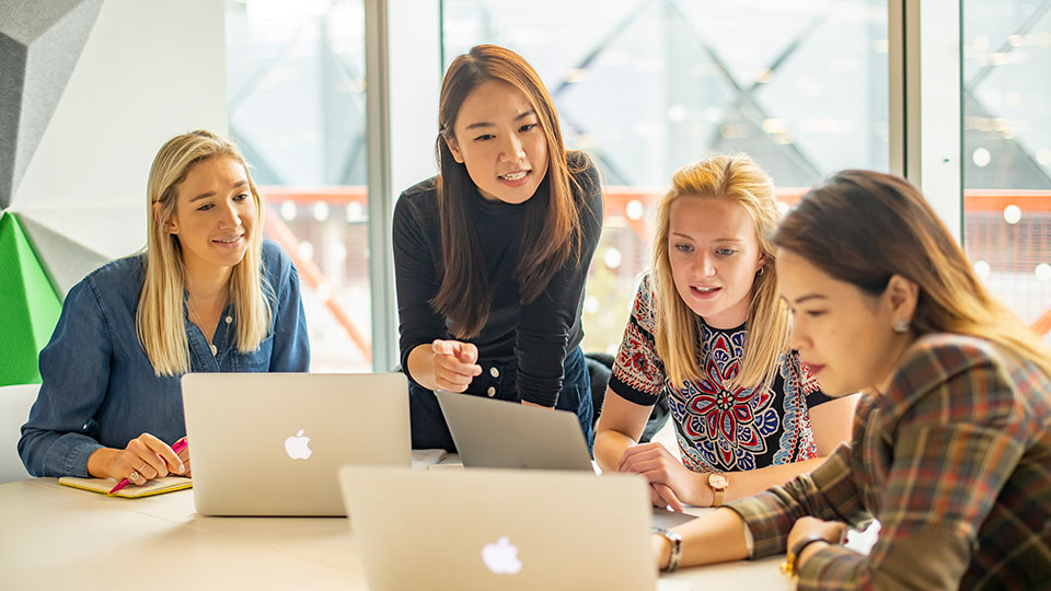Four female students at a table with laptops on it