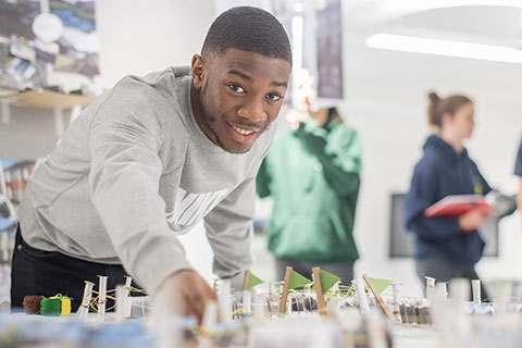 A male student leaning over a desk looking directly at the camera