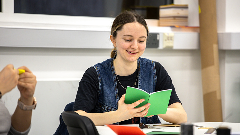 A woman holding a small green book and smiling.