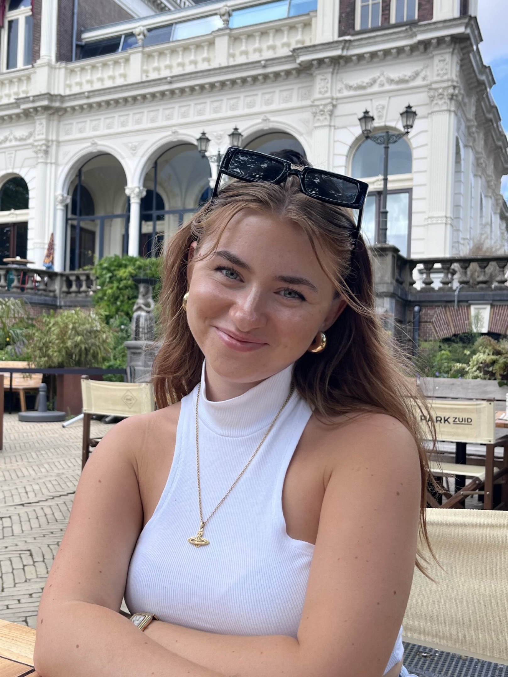 Aimme, a female student with long blonde hair smiles at the camera, she is wearing sunglasses on her head and a white top