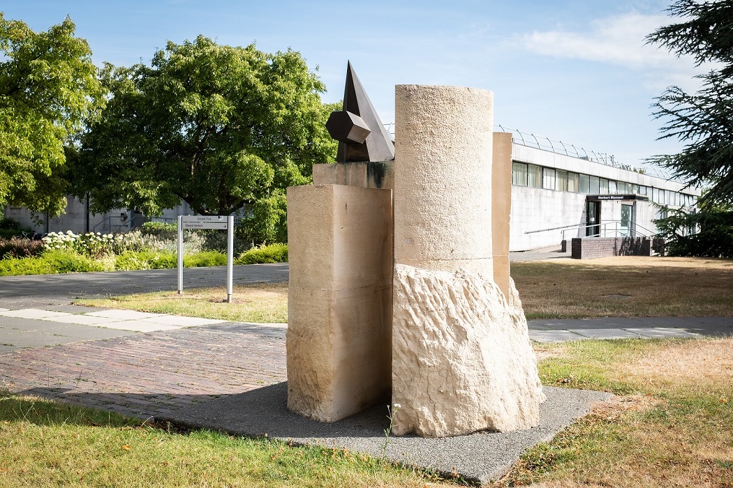 Sculpture with four limestone sections. A brass element is balanced on one of these.