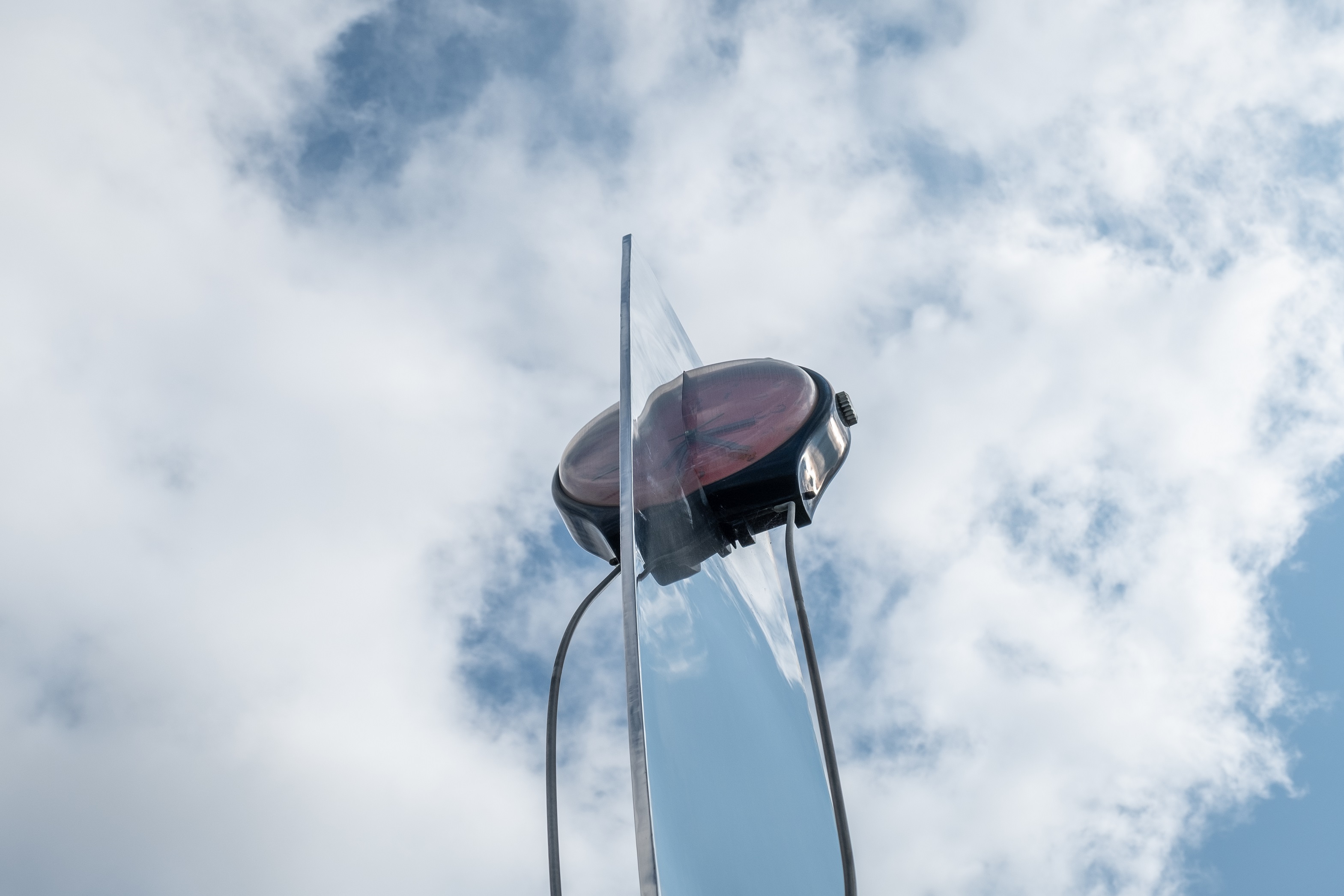 Large 'watch-face' style clock atop angular steel sculpture