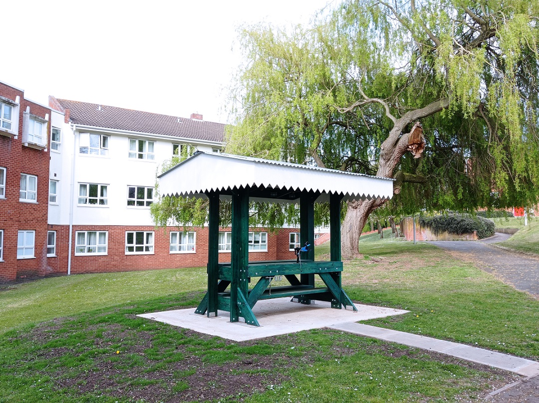 A wooden workbench sculpture in a green area surrounded by buildings