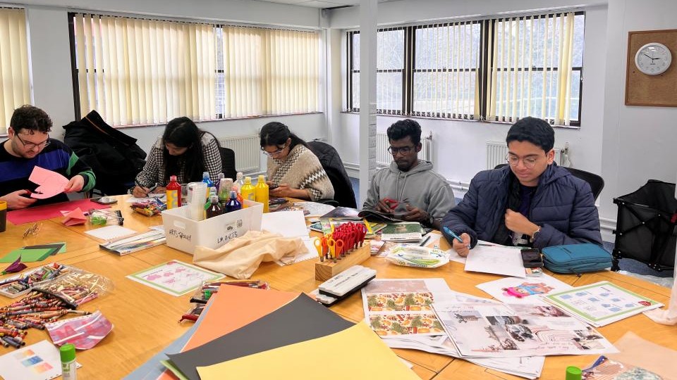 A mixed group of international students sat around a large table creating art