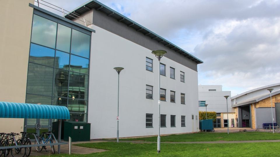 The facade of a modern building with a flat roof and a white wall with lots of small glazed windows and a  fully glazed entrance on the left